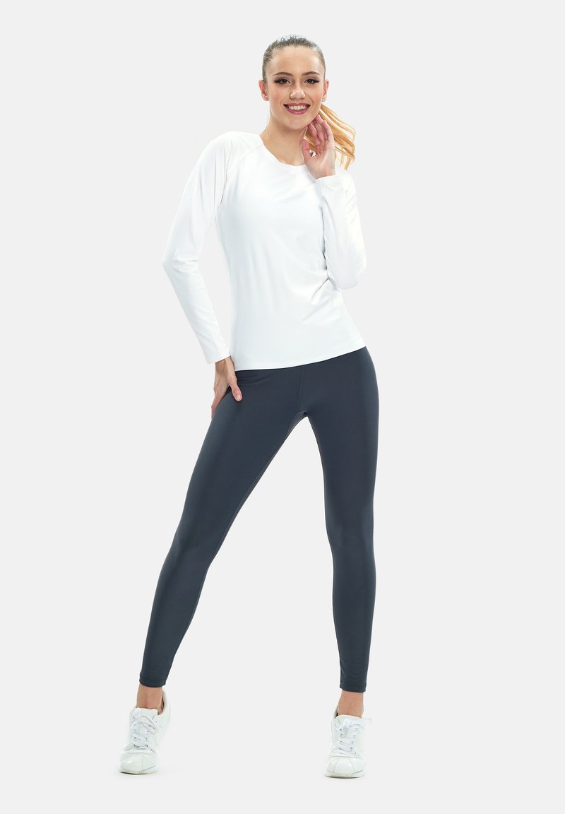Weißes langärmliges Sportshirt, kombiniert mit dunkelgrauen Leggings und weißen Sneakers, mit slim fit und glatter Stofftextur.