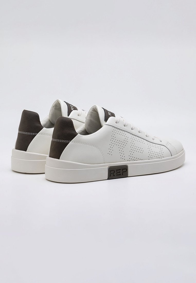 Zapatillas blanca de cuero con detalles perforados, acentos marrón en el talón y una suela de goma texturizada y moldeada. Logo presente en el lateral.