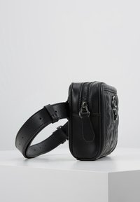 Czarna skórzana torba na ramię z pikowanym wzorem, w kształcie prostokąta, zamykana na zamek błyskawiczny, z regulowanym paskiem. Widoczne akcenty ze srebrnego metalu.