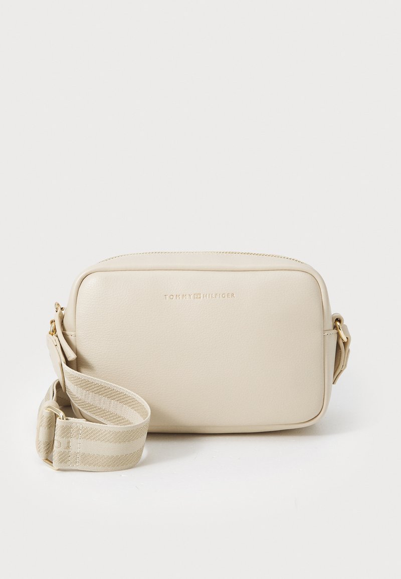 Sac bandoulière en cuir synthétique beige avec une texture douce, quincaillerie dorée et une sangle en tissu rayé. Détails du logo à l'avant.