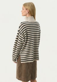 Gestreifter Strickpullover mit hohem Kragen in Beige und Schwarz. Verfügt über gerippte Bündchen und seitliche Schlitze. Kombiniert mit einem braunen Cordrock.