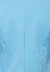 Tissu bleu clair avec une couture verticale au centre, présentant une texture lisse et des surpiqûres discrètes de contour de chaque côté.