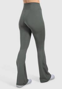 Leggings a vita alta e svasati in tessuto verde scuro. Presentano cuciture flatlock e una texture liscia, progettati per comfort e flessibilità.