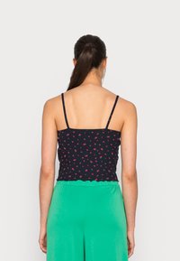 Top curto azul-marinho com pequeno padrão floral, alças finas e bainha em formato ondulado; combinado com calças largas verdes.