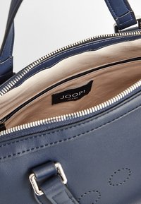 Granatowa skórzana torebka o gładkiej fakturze, ze srebrnym zamkiem błyskawicznym i beżowym wewnętrznym wykończeniem. Wnętrze zawiera metkę "JOOP! JEANS".