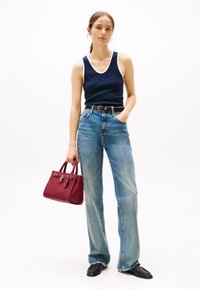 Marinblå linne med vit kant, högmidjade ljusblå jeans och en röd handväska. Modellen bär svarta skor och håller väskan i handtagen.
