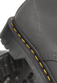 Gros plan sur le talon d'une botte en cuir noire avec des coutures jaunes et une semelle en caoutchouc épaisse et texturée pour la traction et la durabilité.