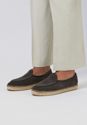Alpargatas sin cordones de ante gris oscuro con suelas de cuerda trenzada, usadas con pantalones cortos de color beige claro.