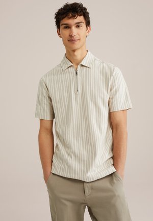 Polo de manga corta en beige con ligeras rayas verticales, con cuello con cremallera y un corte relajado. Fabricado en tejido suave.