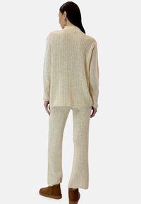 Crème ribgebreide trui met hoge kraag en bijpassende broek. Zachte textuur en losse pasvorm, aangevuld met bruine enkellaarzen.