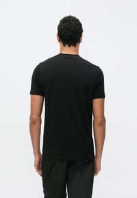 Juoda trumpomis rankovėmis medvilninė marškinėliai su klasikiniu apvaliu kaklu. Lygus audinys ir minimalistinis stilius.