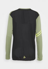 Långärmad sporttröja med gröna ärmar och svart kropp, prydd med reflekterande gula ränder och en logotyp på den nedre delen av ryggen.