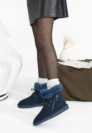 Botas de tobillo de ante azul con un borde de piel, cuello acolchado y cremallera lateral. Llevadas con calcetines blancos a rayas y medias de lunares.