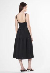 Vestido negro midi con tirantes finos, corsé fruncido y falda en capas. Textura suave y ajuste relajado, diseñado para la comodidad y la facilidad de movimiento.