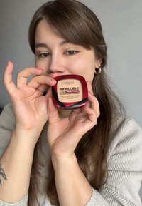 Fond de teint en poudre L'Oréal Infallible 24H Fresh Wear dans un compact rouge carré aux bords arrondis, avec un couvercle transparent et une poudre beige à l'intérieur.