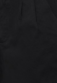 Black cotton fabric with a smooth texture, featuring subtle diagonal lines and a pleated design. Includes a side pocket detail.