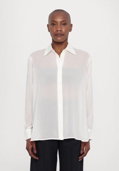 Chemise blanche à manches longues en tissu transparent avec un col pointu, fermeture à boutons et poignets blancs contrastés. Texture douce avec une coupe décontractée.