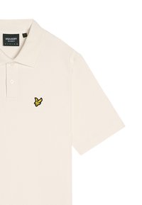Crèmekleurige poloshirt met een zachte textuur, voorzien van een zwart en geel geborduurd vogellogo op de borst en een klassiek kraagontwerp.