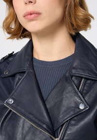 Mörkblå läder motorcykeljacka med silverfärgade dragkedjor och detaljer, utrustad med en bred krage och texturerad stickning under.