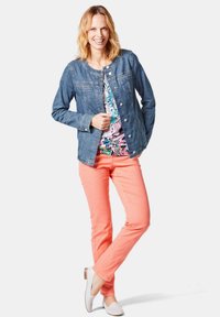 Jeansjacke mit Rundhalsausschnitt, pinkfarbener Bluse darunter und hellrosa Hose. Weiße Ballerinas vervollständigen das Ensemble.