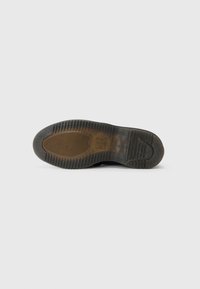 Zwarte sneakersole met getextureerde rubberpatronen, waaronder groeven en een cirkelontwerp. Bevat een klein reliëflogo nabij de hiel.