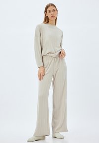 Vaaleanbeige loungewear-setti, jossa on löysä pitkähihaisista paita ja leveälahkeiset housut, joissa on teksturoitu kuvio ja joustava vyötärö.
