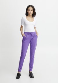 Paarse joggingsbroek met een trekkoord in de taille, voorzien van zijzakken en een slim fit. Gecombineerd met een witte, aansluitende t-shirt met korte mouwen en zwarte instapschoenen.