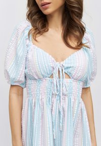 Light blue and pastel striped dress with puffed sleeves, a tie-front detail, and gathered waistband; features a relaxed fit and playful pattern.