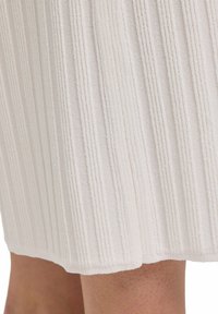 Teksturowana tkanina w kolorze off-white z pionowymi paskami, miękki materiał i lekko nieregularny dół, sugerujący luźny krój.