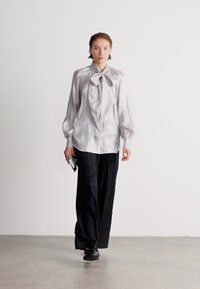 Light gray satin blouse with a bow tie collar, paired with black wide-leg trousers and black shoes, on a model against a plain background.
