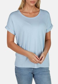 Camiseta de manga corta azul claro con escote redondo, de tejido suave, mangas enrolladas y corte relajado. Combinada con jeans de mezclilla.