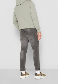 Sudadera gris clara con un bolsillo canguro, combinada con jeans gris ajustados. Los zapatos son multicolores con una suela moteada y cordones blancos.