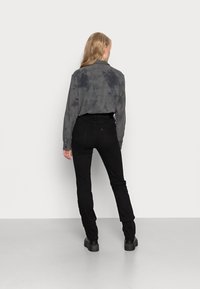 Gray tie-dye shirt with long sleeves paired with black skinny jeans and platform boots, viewed from the back against a plain background.