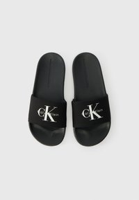Μαύρα σχέδια σάνδαλα με μαλακή υφασμάτινη ταινία που διαθέτει το λογότυπο "CK" σε λευκό χρώμα. Η σόλα είναι υφή, κατασκευασμένη από ανθεκτικό υλικό για άνεση.