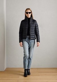 Doudoune noire avec un matelassage horizontal, fermeture éclair, associée à un haut noir ajusté, un jean bleu clair et des bottines noires.