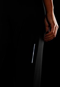 Czarne sportowe spodnie o dopasowanym kroju z refleksyjnym srebrnym akcentem po bokach. Materiał wydaje się gładki i lekko elastyczny.