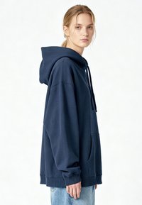 Tengerészkék színű, bő fazonú pulóver kapucnival, pamutkeverék anyagból készült, elülső zsebbel, húzózsinóros kapucnival, valamint bordázott mandzsettákkal és szegéllyel.