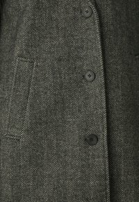 Cappotto a zig zag in tessuto nero e crema. Presenta cinque bottoni neri e una tasca laterale per funzionalità.