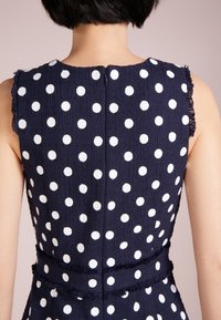Námořnické šaty s bílými puntíky, texturovaná tkanina, bez rukávů, se zadním zipem a třásňovými detaily na lemu.