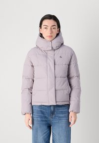 Svijetlo lavanda puffer jakna s visokim ovratnikom, prednjim zatvaranjem i kvadratnim uzorkom. Ima bočne džepove i logo na prsima.