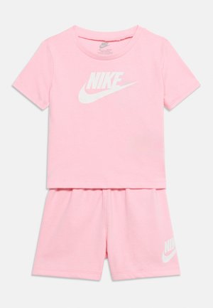 Rózsaszín Nike rövid ujjú póló és hozzá illő rövidnadrág fehér Nike logóval a mellkason és a bal lábon, fehér háttéren laposan bemutatva.