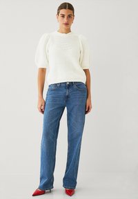 Pull bianco lavorato a maglia con maniche a sbuffo, abbinato a jeans dritti blu chiaro e décolleté rosse a punta. Collo semplice e tessuto testurizzato.