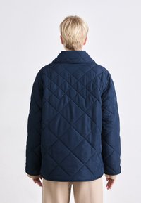 Navy quilted jacket featuring a wide collar, diamond pattern, and contrasting beige cuffs. Soft texture with a relaxed fit.