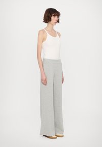 Lichtgrijze, wijde broek van zacht, gebrusht stof met een gladde tailleband, gecombineerd met een aansluitend wit tanktop.