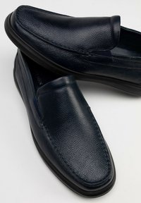 Marineblauwe leren instappers met een gestructureerde afwerking, ronde neus en contrasterende stiksels. Voorzien van een flexibele zwarte rubberen zool.