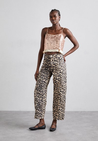 Haut en sequins rose doré court avec bord crème, associé à un pantalon large en imprimé léopard beige. Le mannequin porte des ballerines noires. Fond neutre.