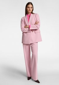 Completo su misura rosa composto da un blazer con design doppiopetto e pantaloni a gamba larga, abbinato a una camicia rosa brillante e scarpe scure.