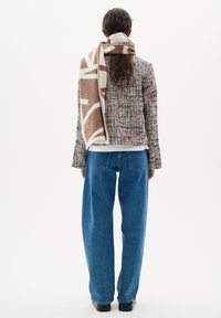Eșarfă din amestec de lână, de culoare maro și crem, așezată peste o jachetă din tweed multicolor, asortată cu blugi lejeri de culoare albastră și încălțăminte neagră.