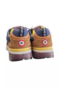 Un paio di sneakers multicolori con tacco in suede, emblema circolare rosso-bianco-verde, finiture gialle, linguetta nera sul tallone con testo bianco e suola scura.