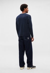 Jūras flotes džemperis ar apaļu kakla izgriezumu un kontrastējošu šuvju apdari, kopā ar vaļīgām tumšām džinsa biksēm ar aizmugurējā kabatas logo. Ikdienas apavi papildina izskatu.